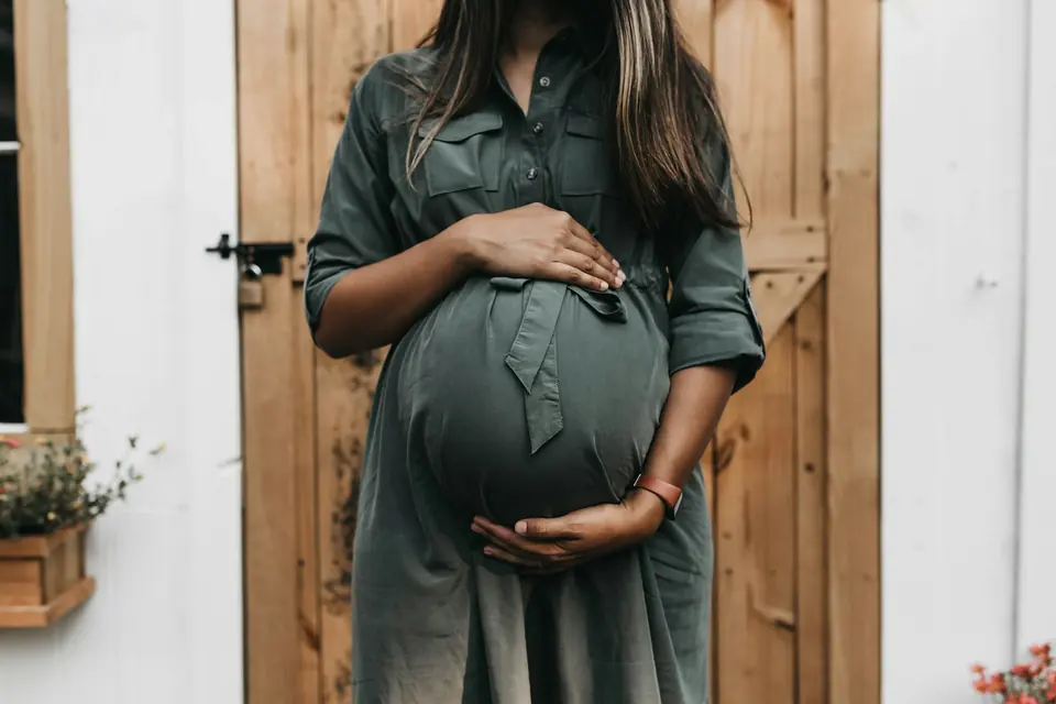 Gravid kvinne i grønn kjole holder rundt magen foran en tredør