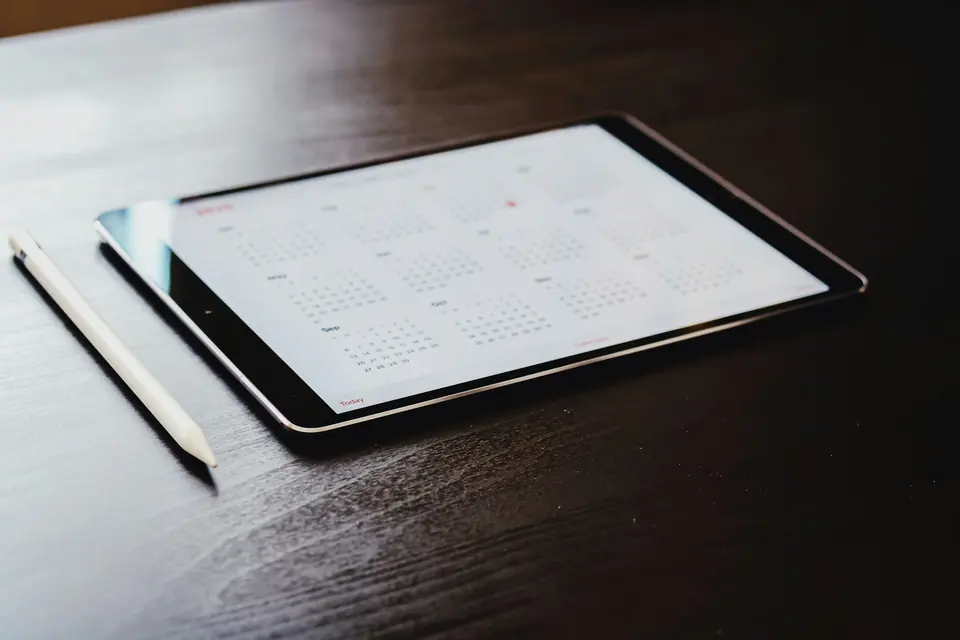 Nettbrett med årskalender på skjermen og en hvit pekepenn på et mørkt trebord