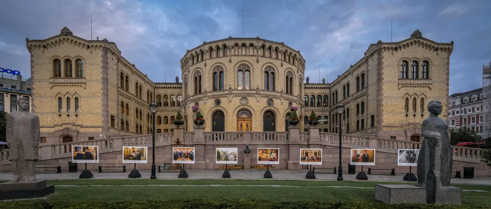 Stortingsbygningen i Oslo i kveldslys, med plen og statuer foran fasaden