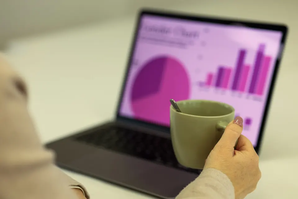 Hånd med kaffekopp foran en bærbar PC som viser kake- og stolpediagram